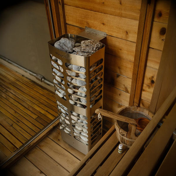 Vented sauna heater with gray rocks in a stainless stone basket inside a wooden sauna