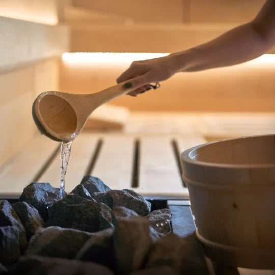 Person pouring water from a wooden ladle into a container in a warm indoor setting. Golden Designs