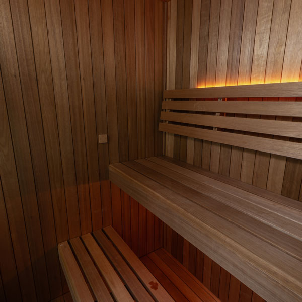 Wood sauna interior corner with two-tier bench seating and warm overhead lighting