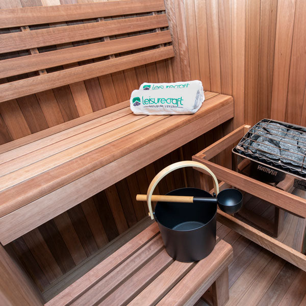 Wooden sauna bench with folded towel, sauna bucket ladle, and heater box