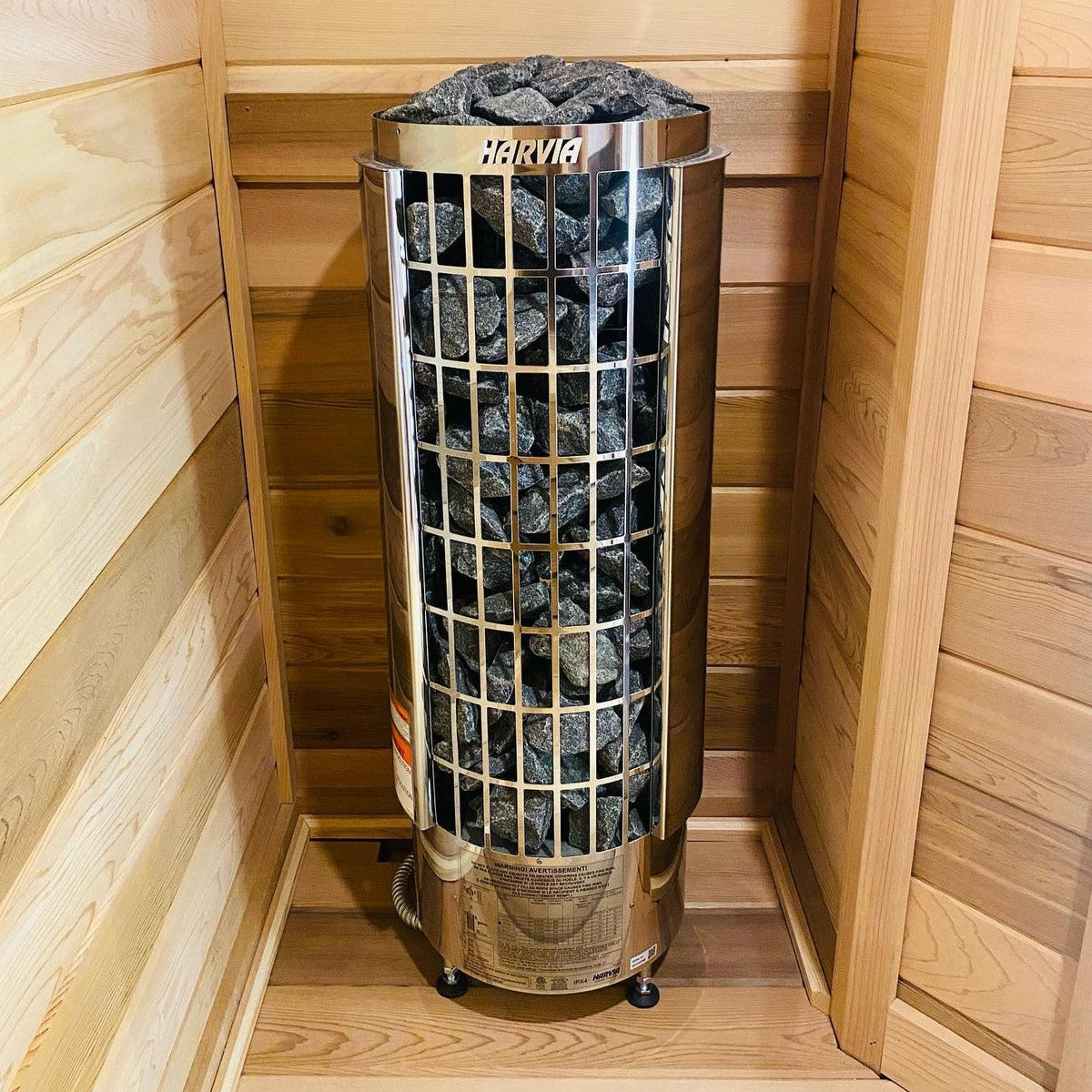 Cylindrical sauna stove heater filled with rocks, mounted inside wood sauna enclosure