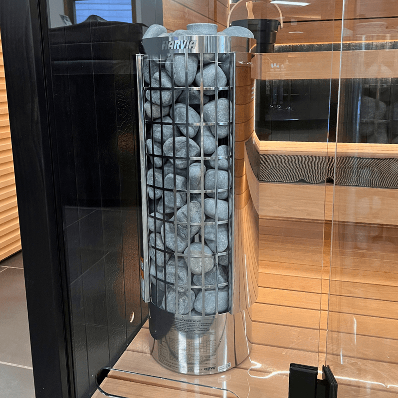 Harvia stainless sauna heater with stone-filled grid cylinder near glass wall