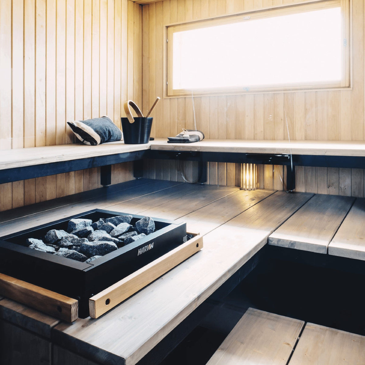 Electric sauna heater with black firebox and wood base, filled with dark stones