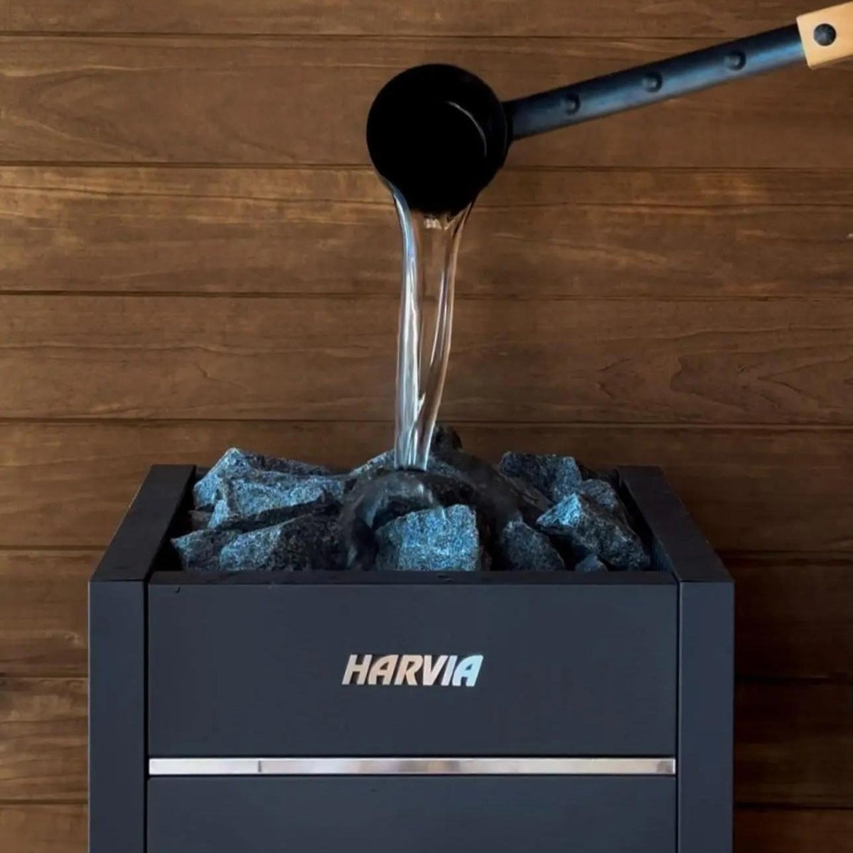 Electric sauna heater pouring water onto dark stones in black tray