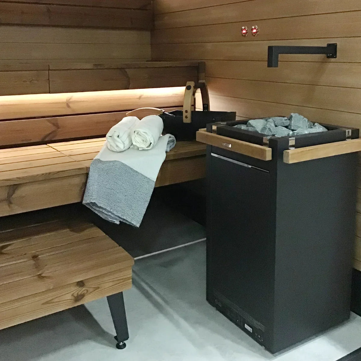 Electric sauna heater beside bench in sauna, dark cabinet with stone-filled top tray