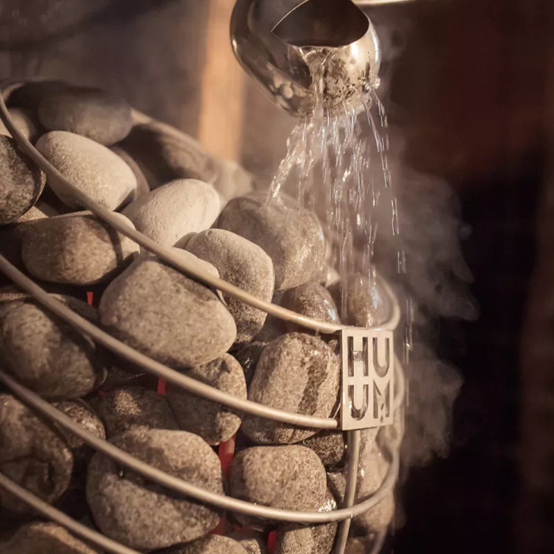Water pouring onto grey sauna stones with steam rising from the heater