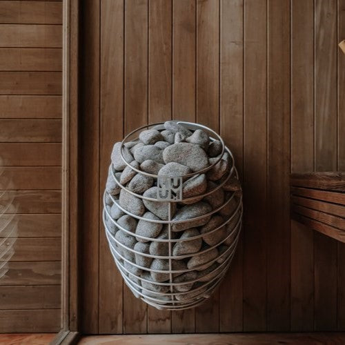 Sauna heater filled with grey stones against a wooden wall