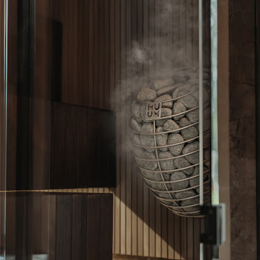 Sauna heater with grey stones behind a glass panel with visible mist