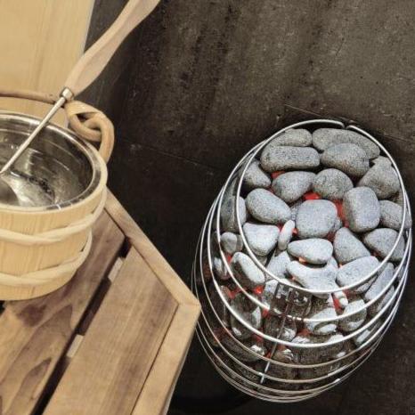 Electric sauna heater holding gray stones with ladle nearby