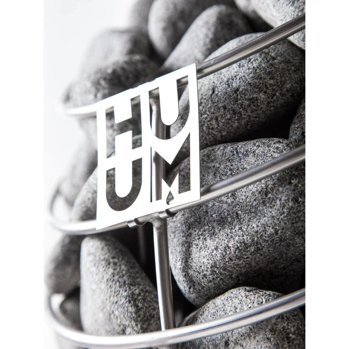 Close-up of HUUM logo on gray sauna stones in a wire heater basket