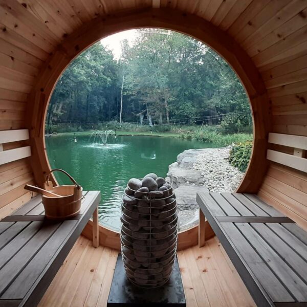 Sauna heater with stacked gray stones beside window opening, rock basket on floor