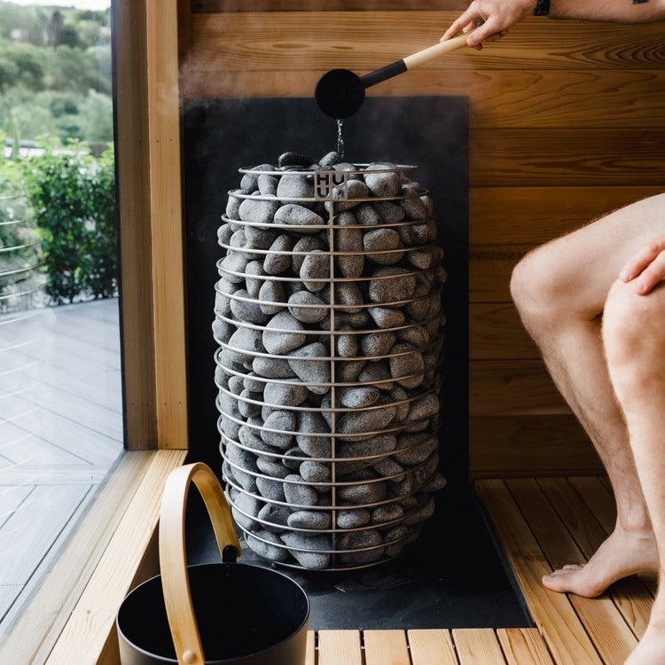 Sauna heater with stacked gray stones while water pours from a ladle onto rocks