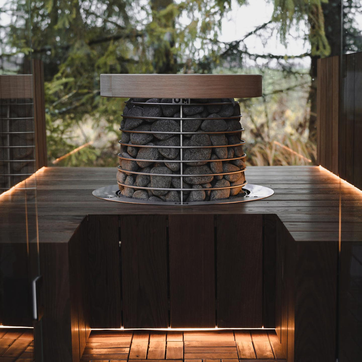 Round outdoor sauna heater with stacked gray stones inside a metal cage