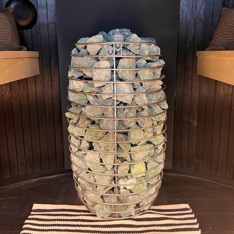 Electric sauna heater packed with gray stones in a wooden cabin