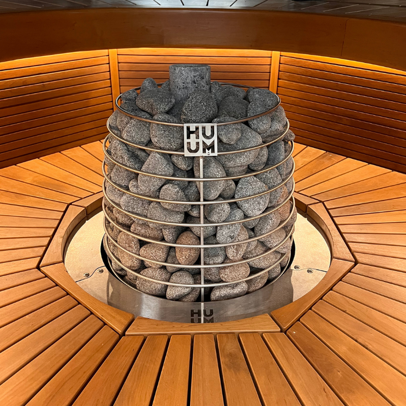 Electric sauna heater filled with gray stones inside a wooden sauna