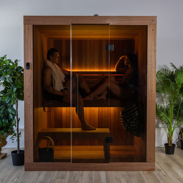 Front view of wood sauna with glass door and two people seated on benches