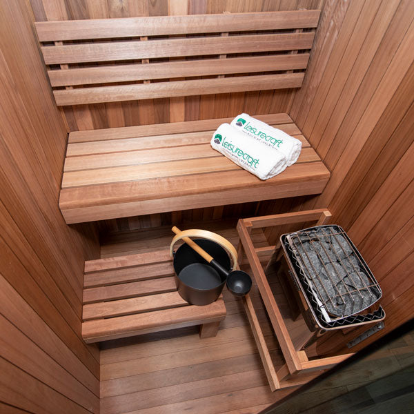 Wooden sauna with upper bench, folded towel, bucket and ladle, and heater compartment