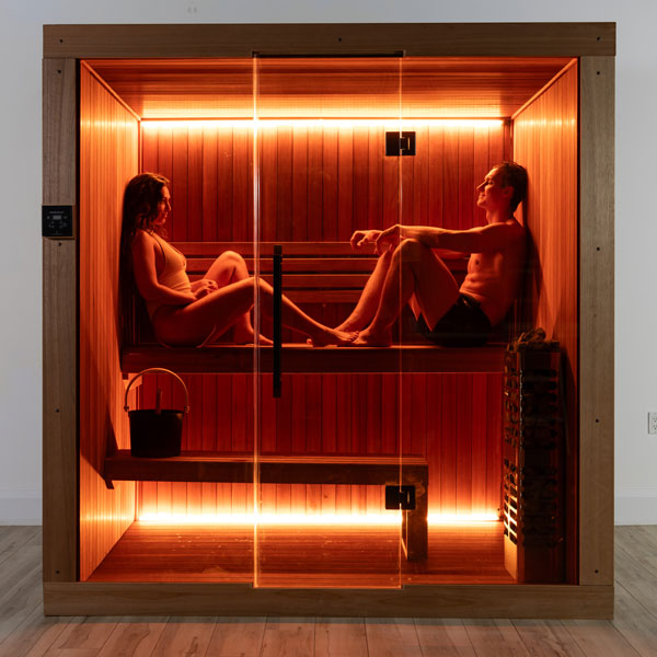 Wooden sauna with glass door, two-tier benches, and heater with warm interior lighting.