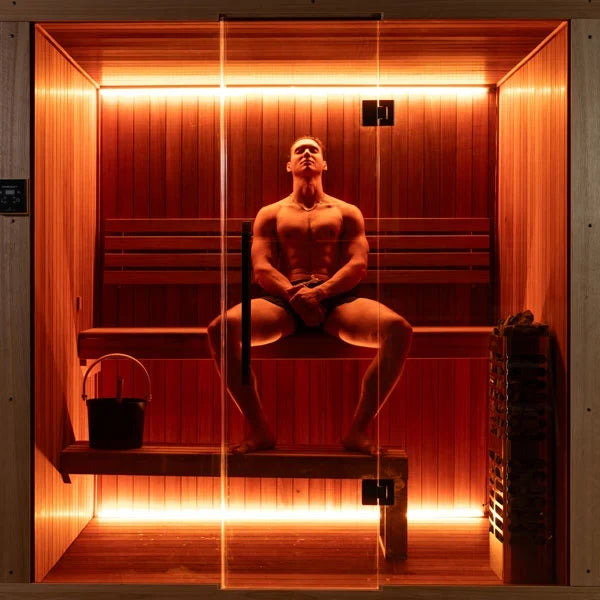 Studio sauna interior with seated person, wooden benches, warm light strips, and wall panels.
