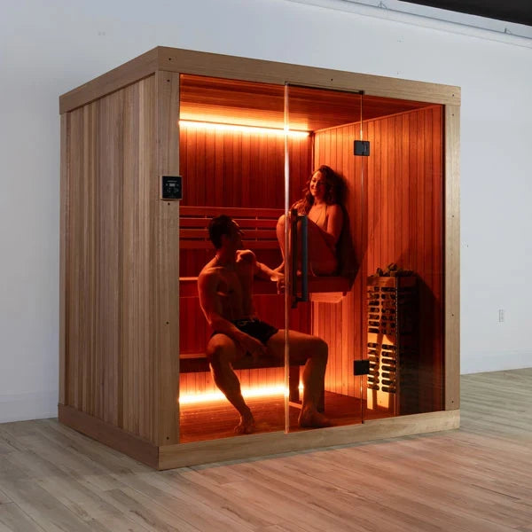 Corner view of wooden studio sauna with glass door, glowing interior benches and heater.