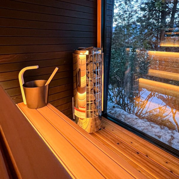 Harvia sauna heater with ladle pouring water beside window in sauna