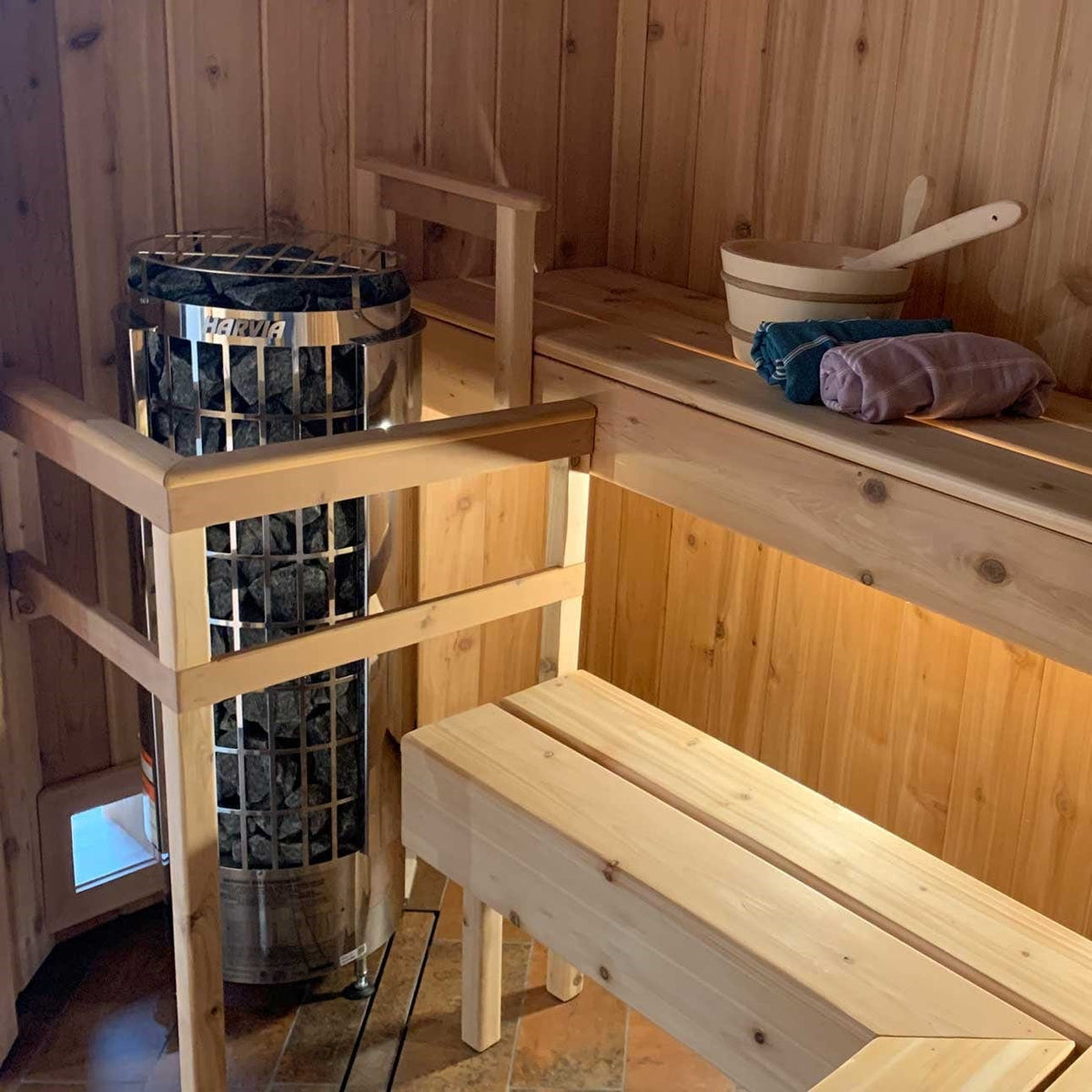 Compact sauna heater cylinder in a wooden sauna with stone basket and cover
