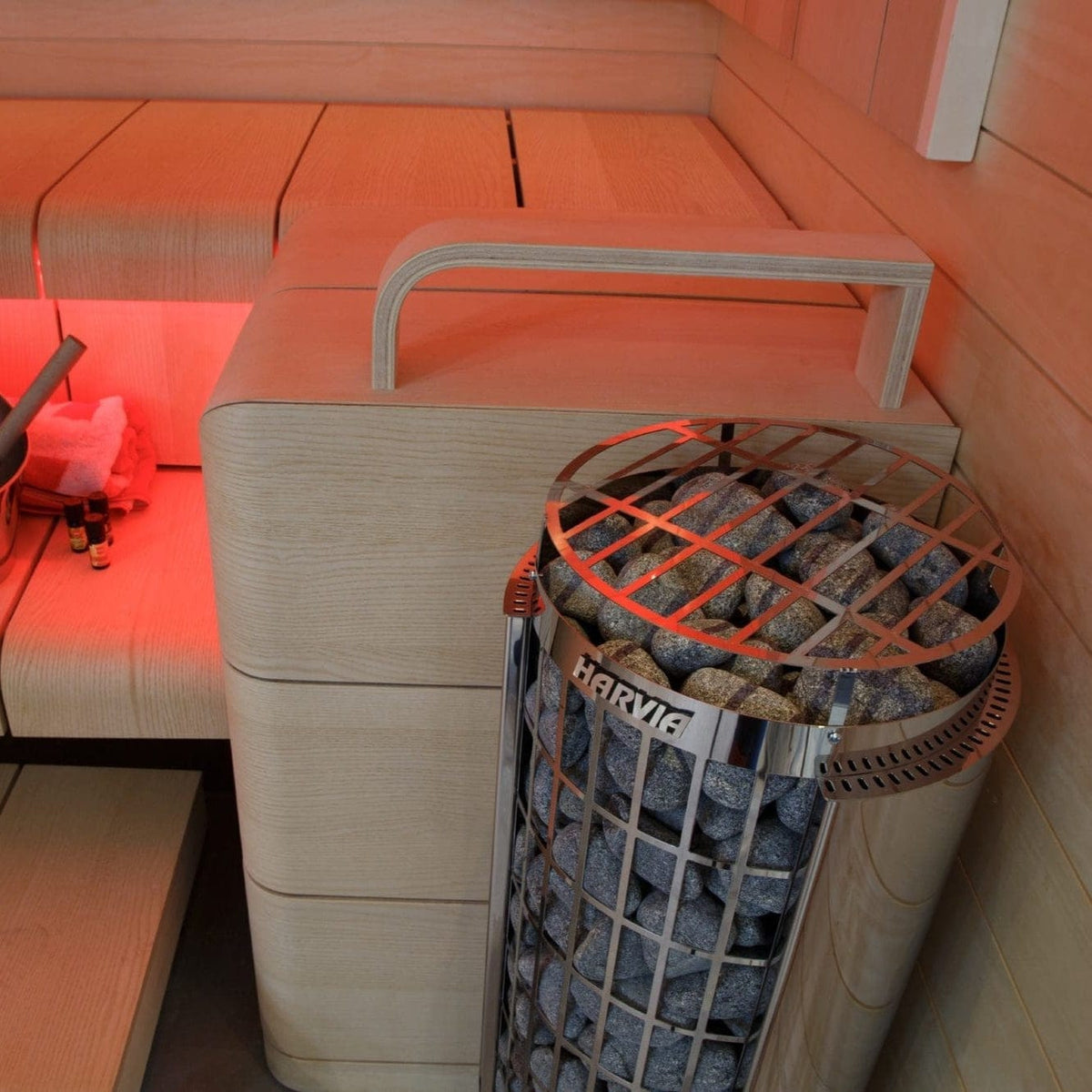 Sauna heater cylinder with rocks inside, set near bench seating with red light glow