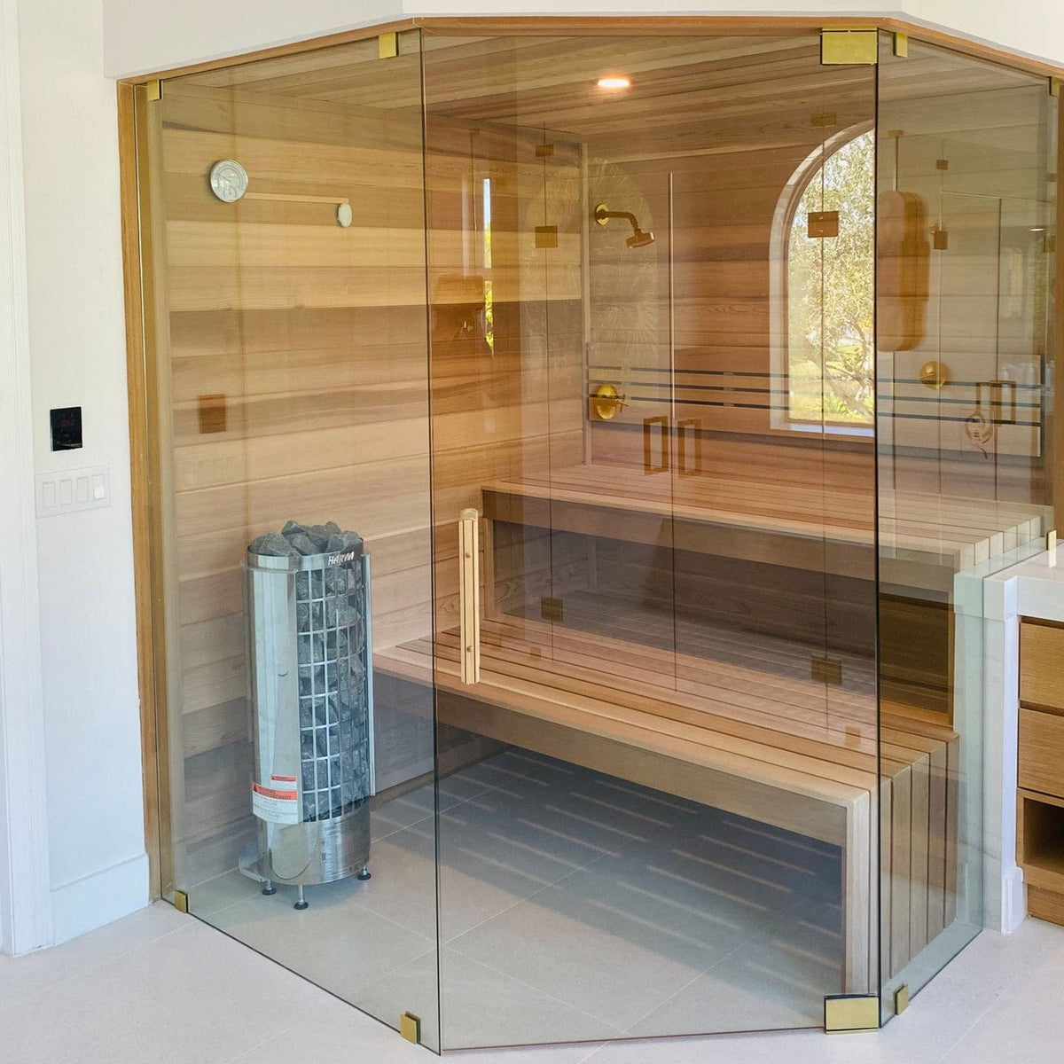 Cylindrical sauna heater with metal stone basket installed in a glass sauna enclosure