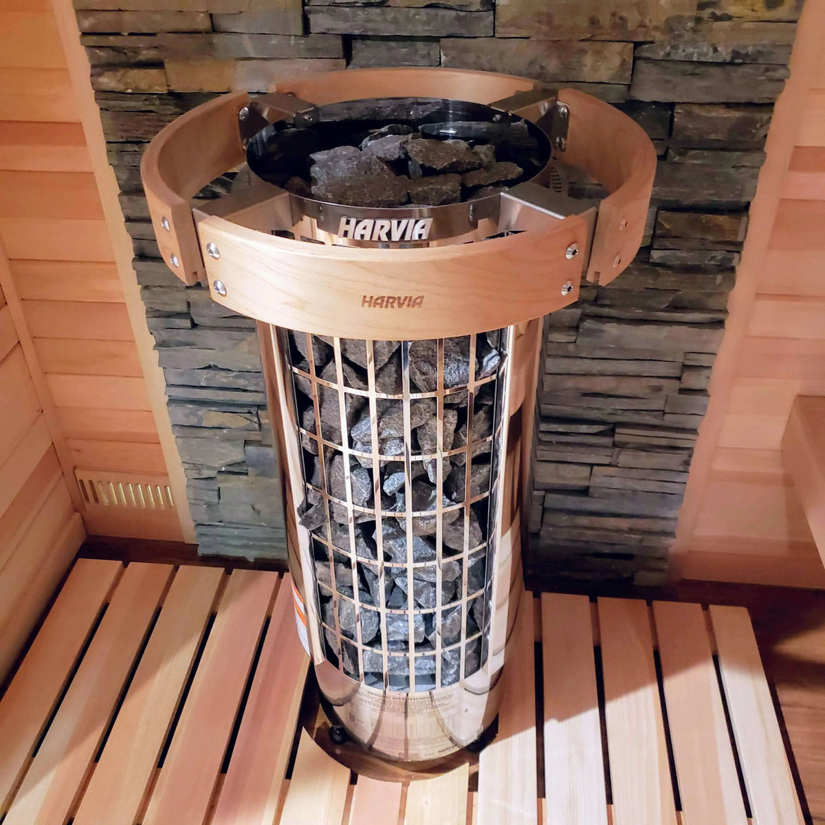 Top view of cylindrical sauna heater with rocks inside, mounted against stone wall