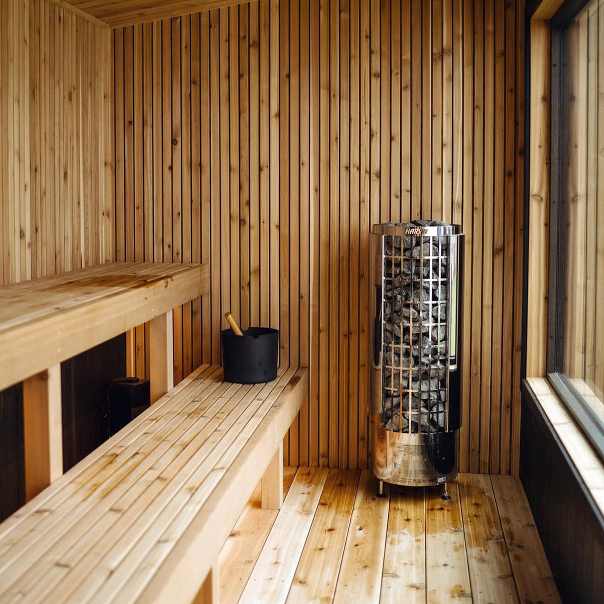 Cylindrical sauna heater with metal stone cage and stove top in a wooden sauna