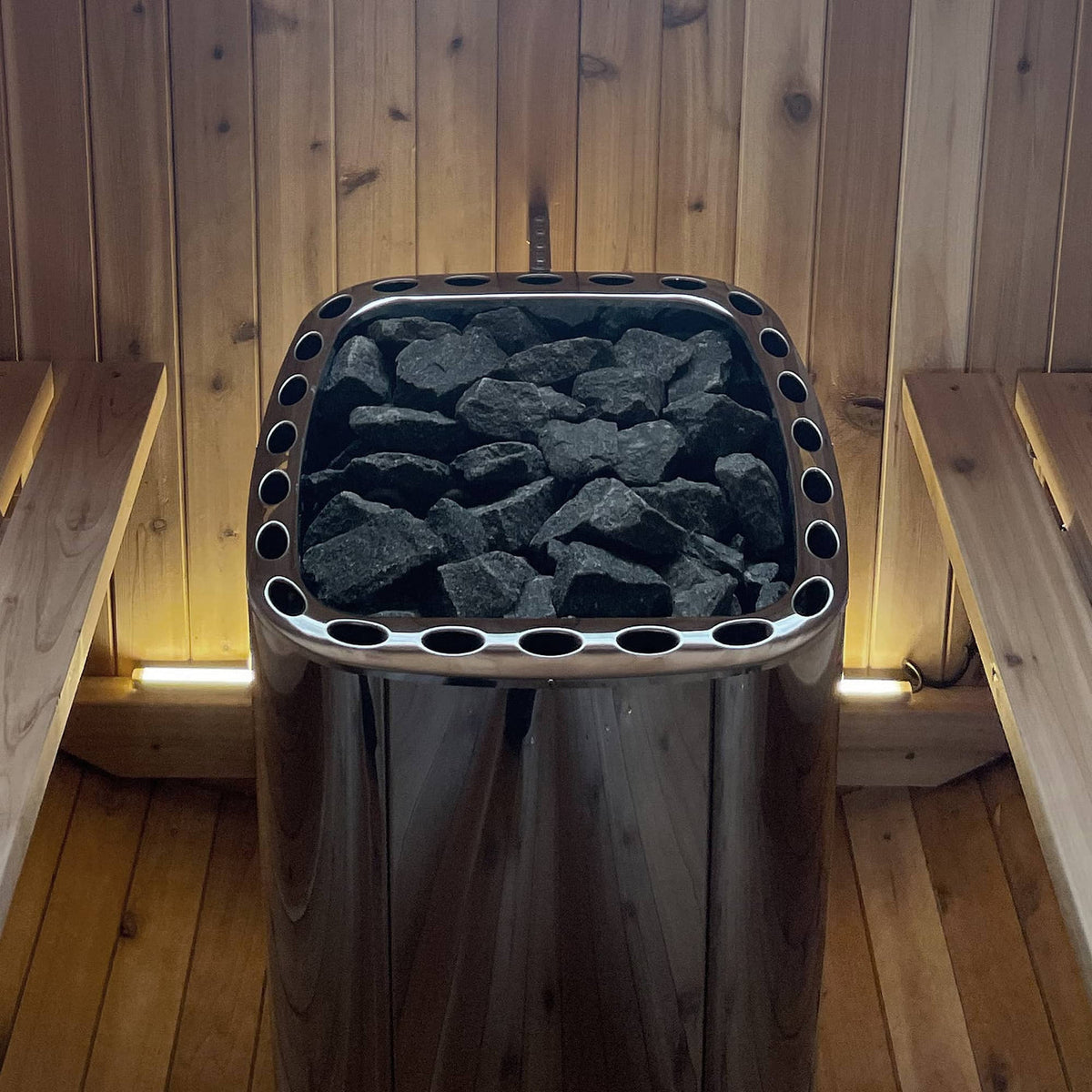 Electric sauna heater filled with dark stones, with circular vent holes around the frame