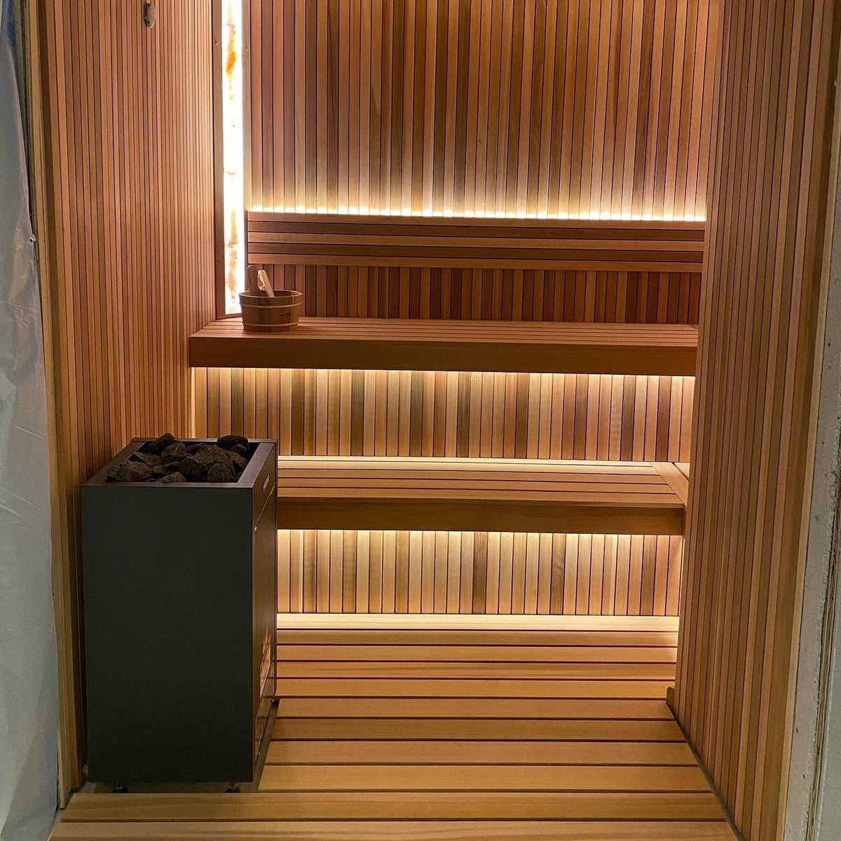Dark gray sauna heater with stones on top in a wooden sauna room