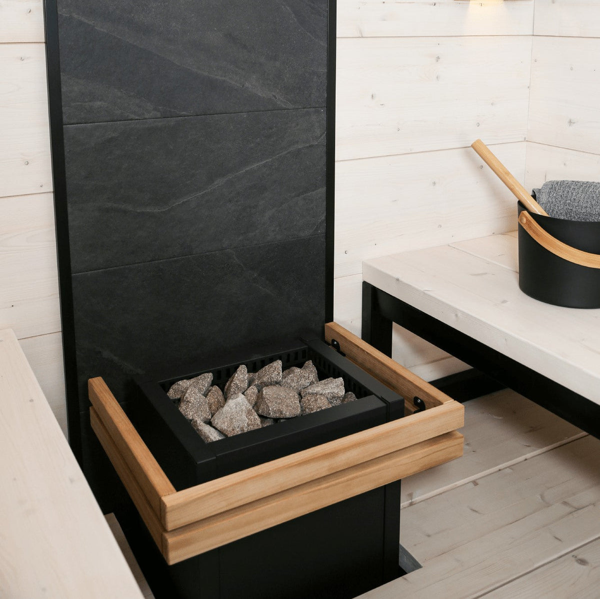 Black sauna heater with wooden rim holding grey sauna rocks