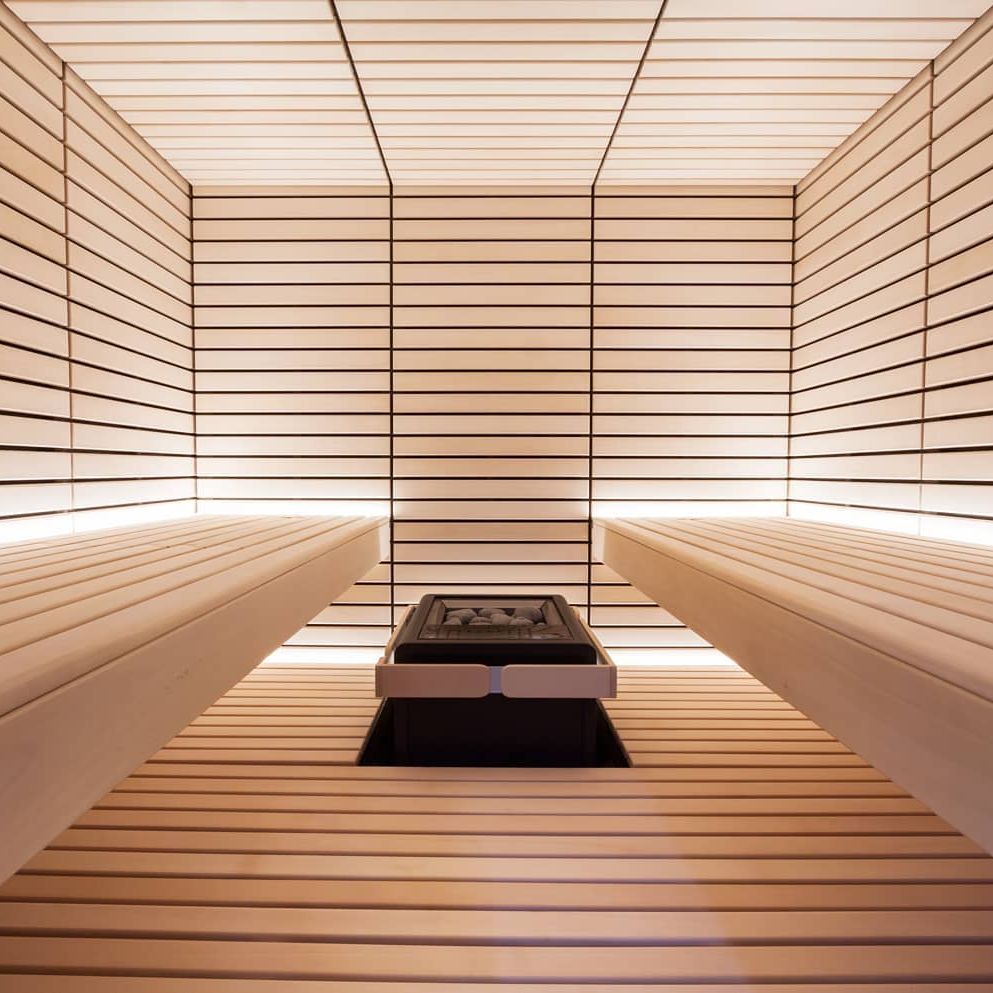 Electric sauna heater centered in sauna with stone tray visible between wooden benches