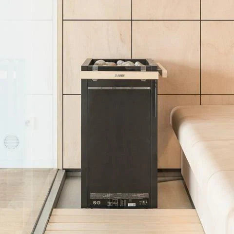 Dark gray electric sauna heater with open stone top in a tiled sauna nook