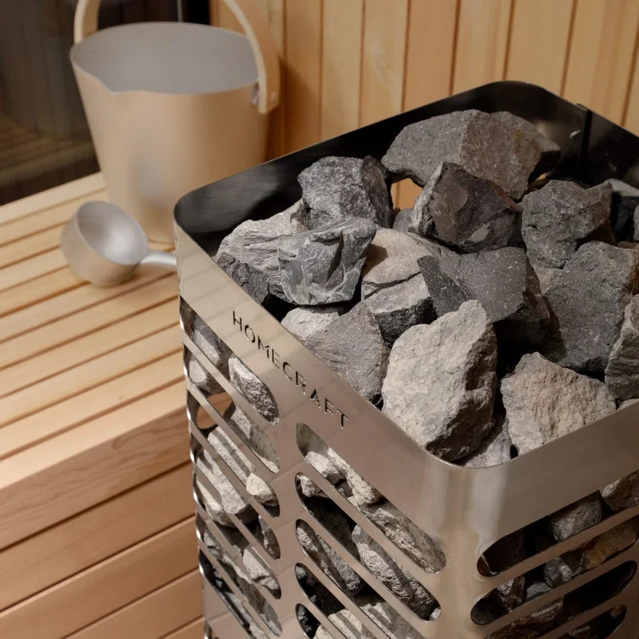 Electric sauna heater filled with gray and black rocks in a stainless steel firebox