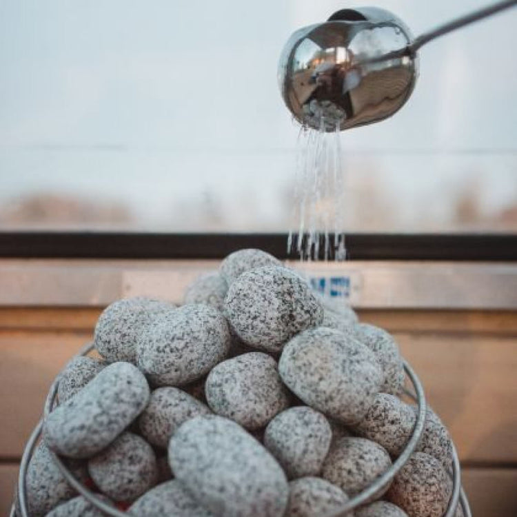 Metal electric sauna heater filled with gray stones as water pours over