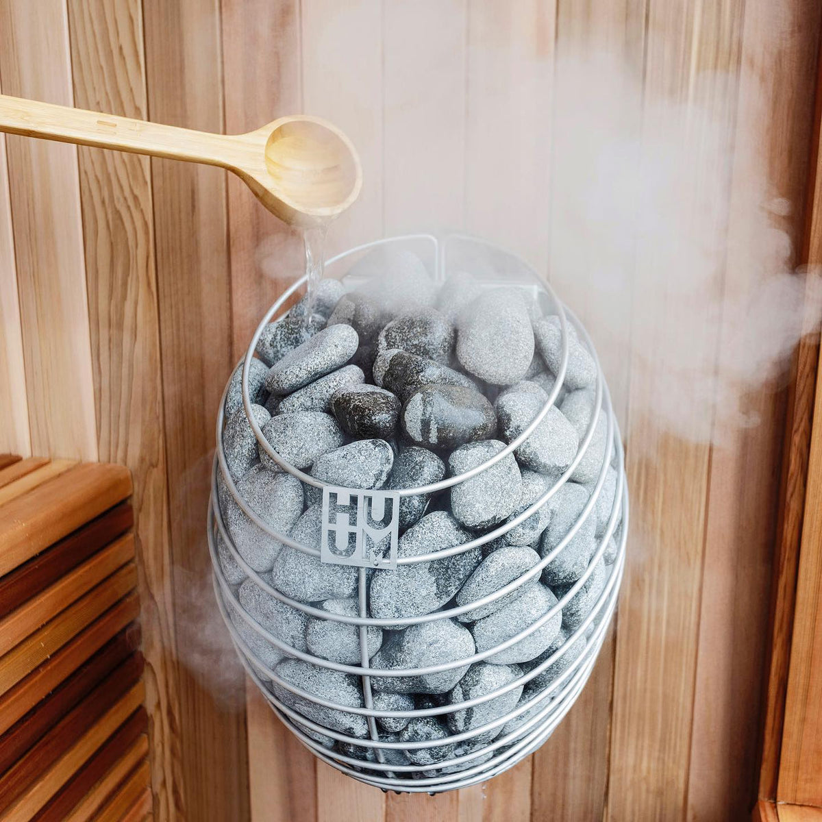 Electric sauna heater with gray stones in metal basket and visible steam
