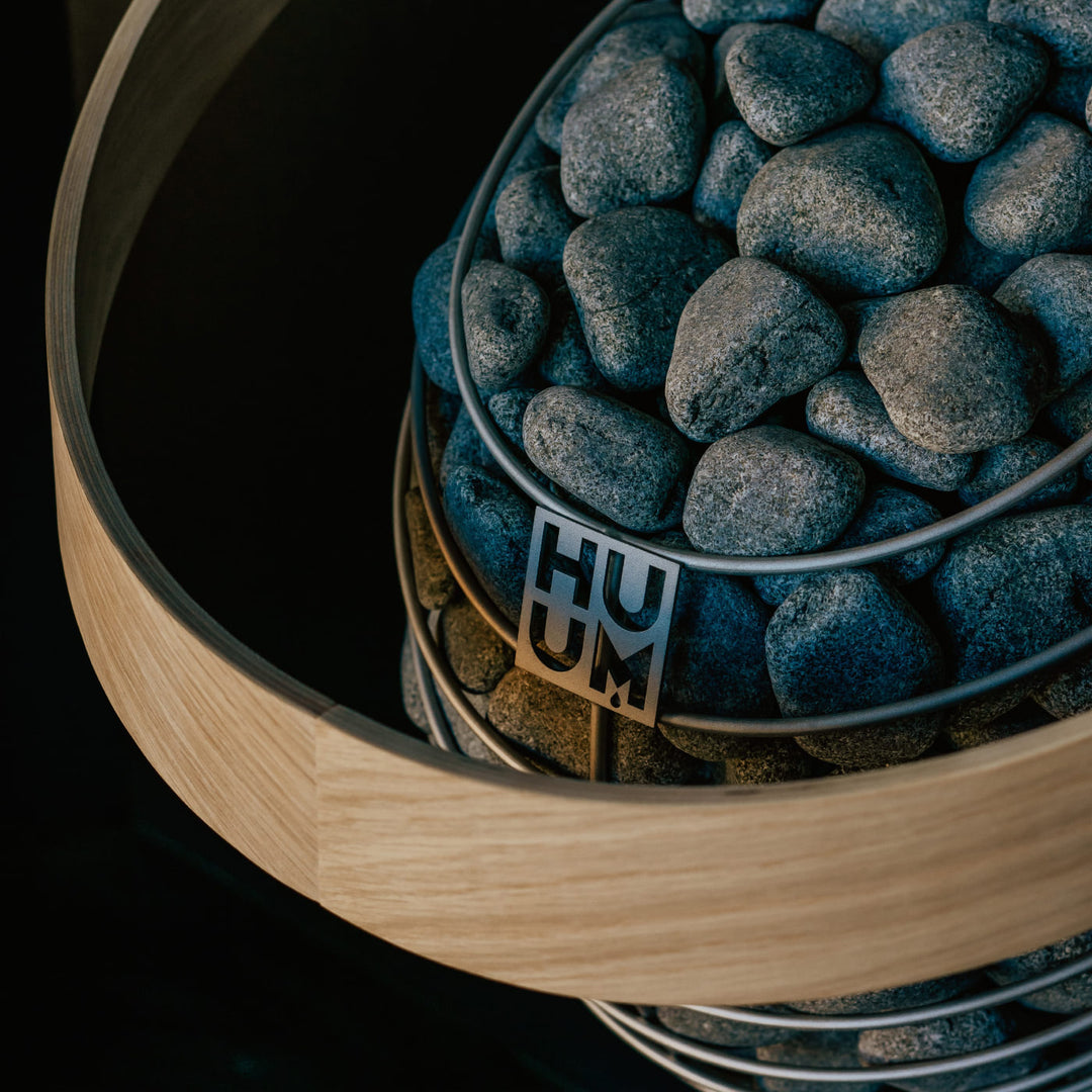 Close-up of HUUM sauna heater stones with wire rim and metal support