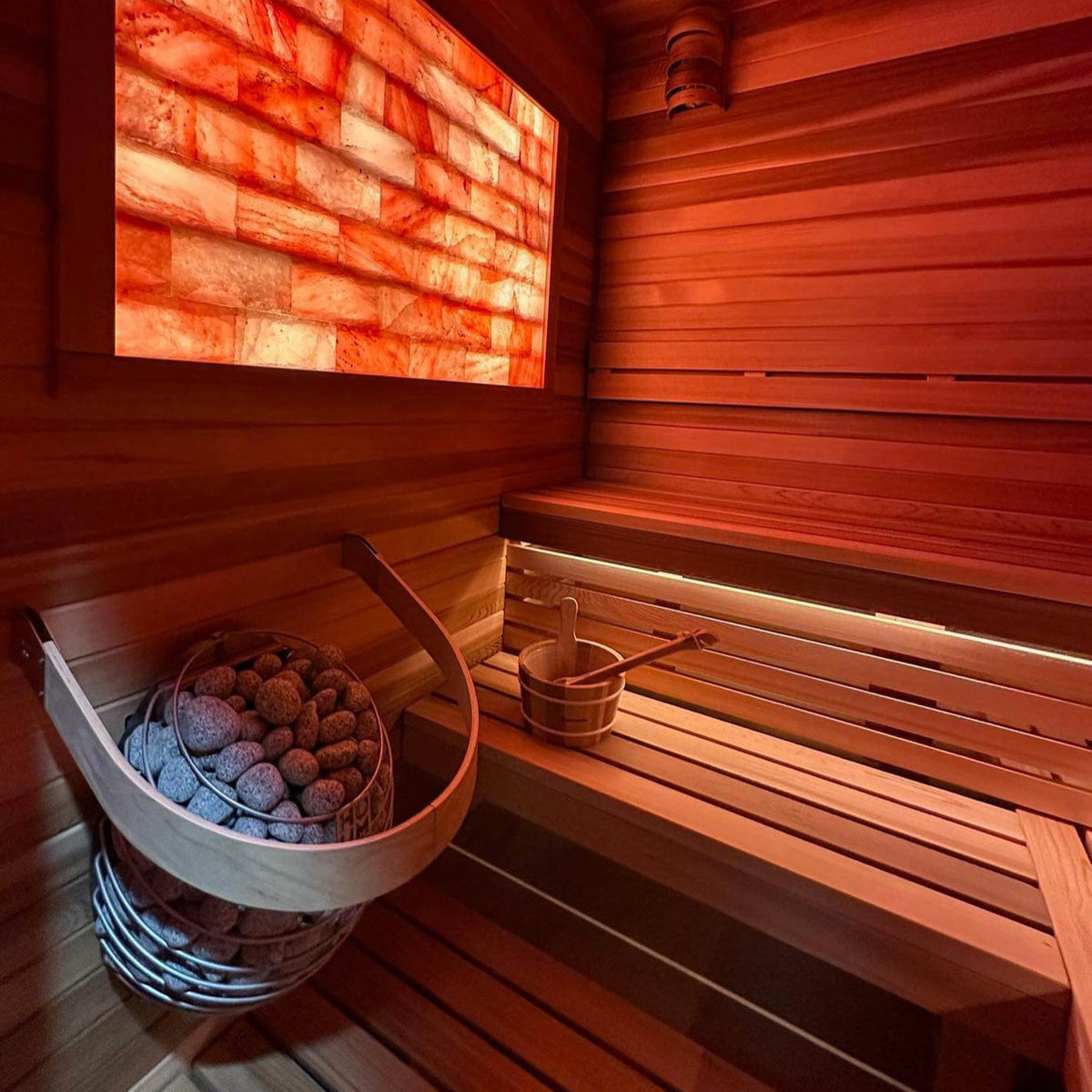 HUUM sauna heater stone basket with gray rocks beside wooden bench