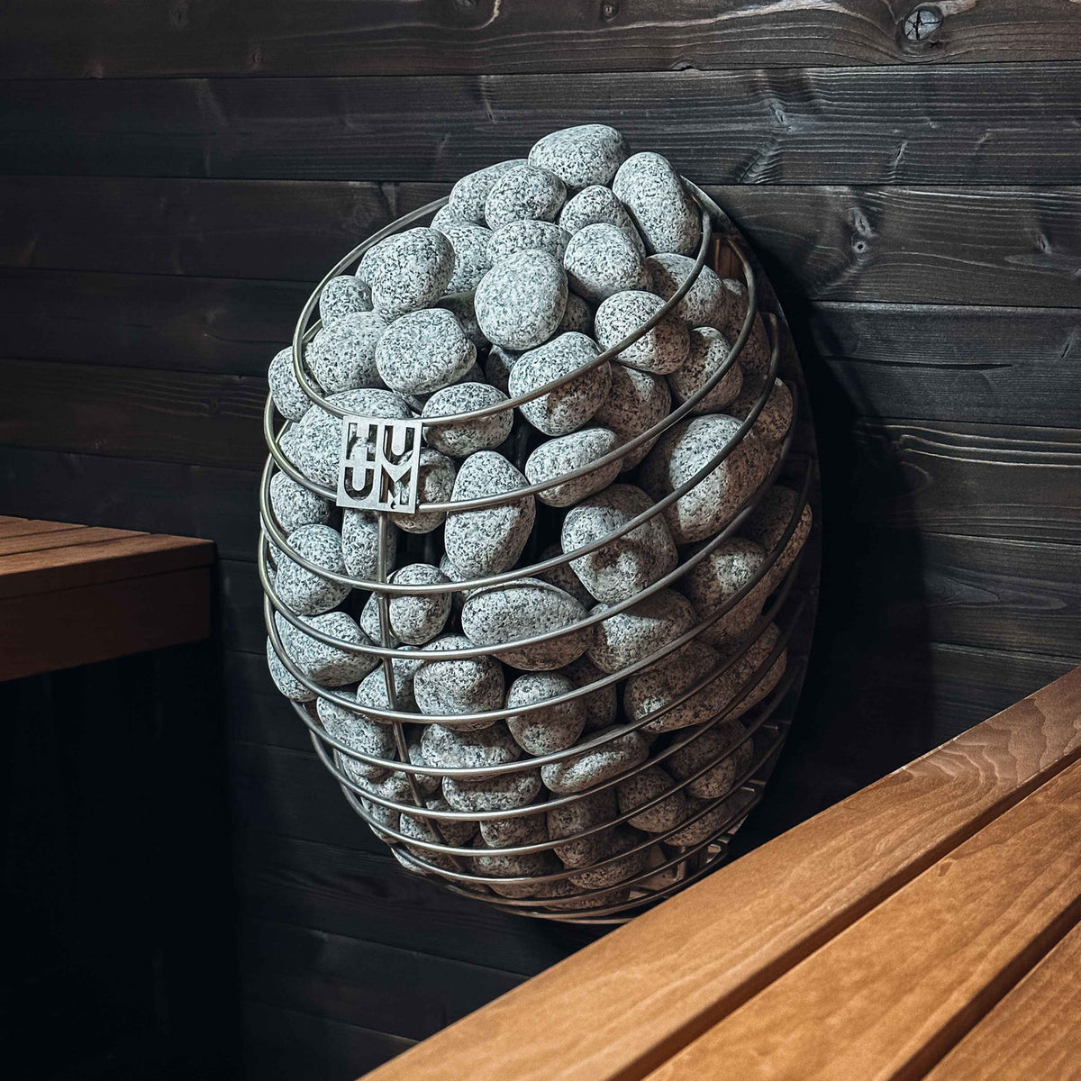 HUUM sauna heater with gray stones stacked in a wire cage basket