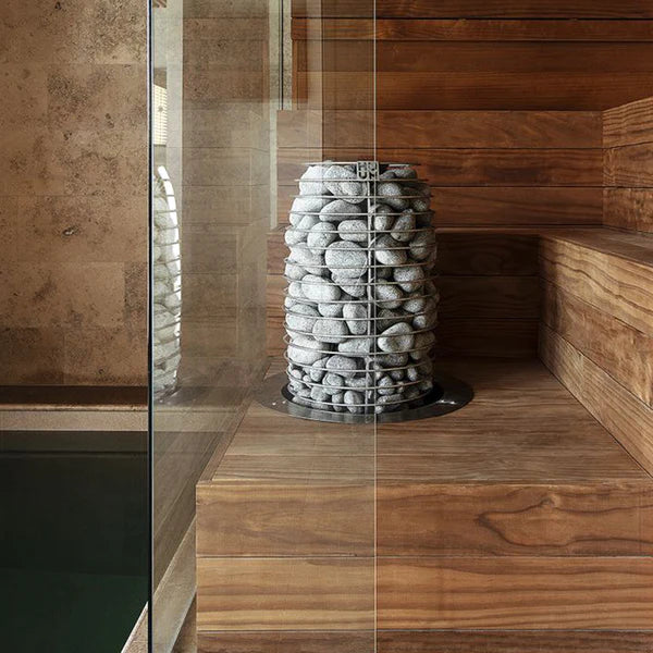 Tall electric sauna stone heater with stacked light gray rocks beside a glass panel