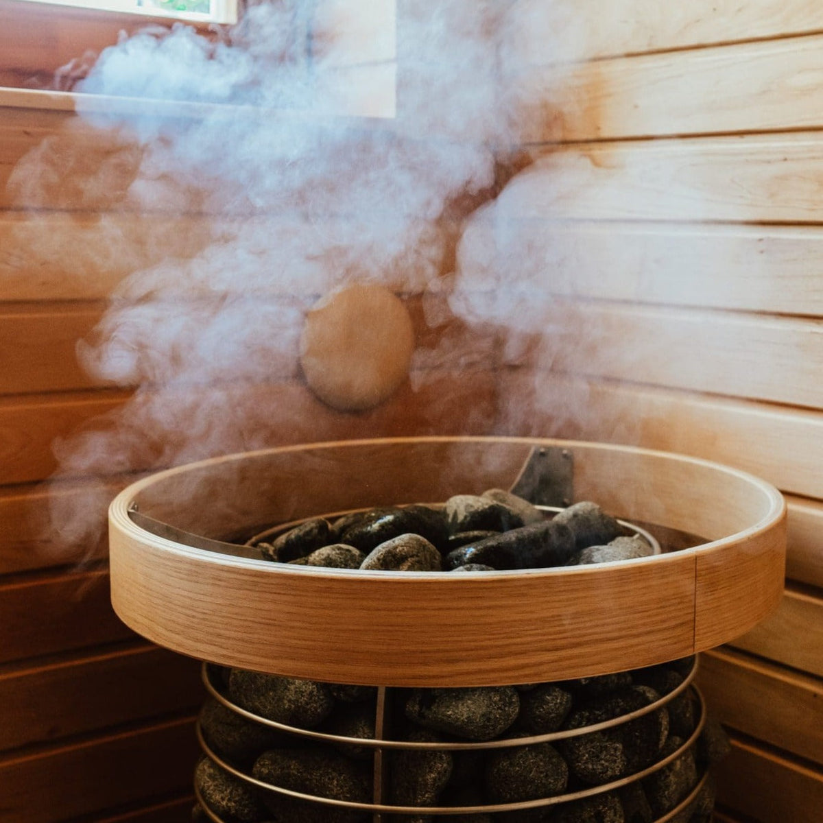 Steaming sauna heater stone basket with gray stones in a circular metal holder