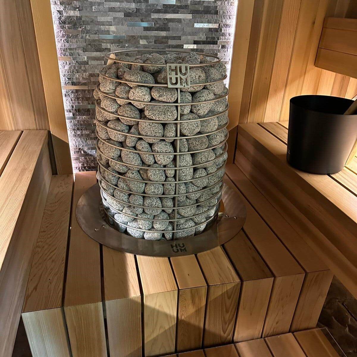 Electric sauna heater with light green stones and HUUM label in a sauna