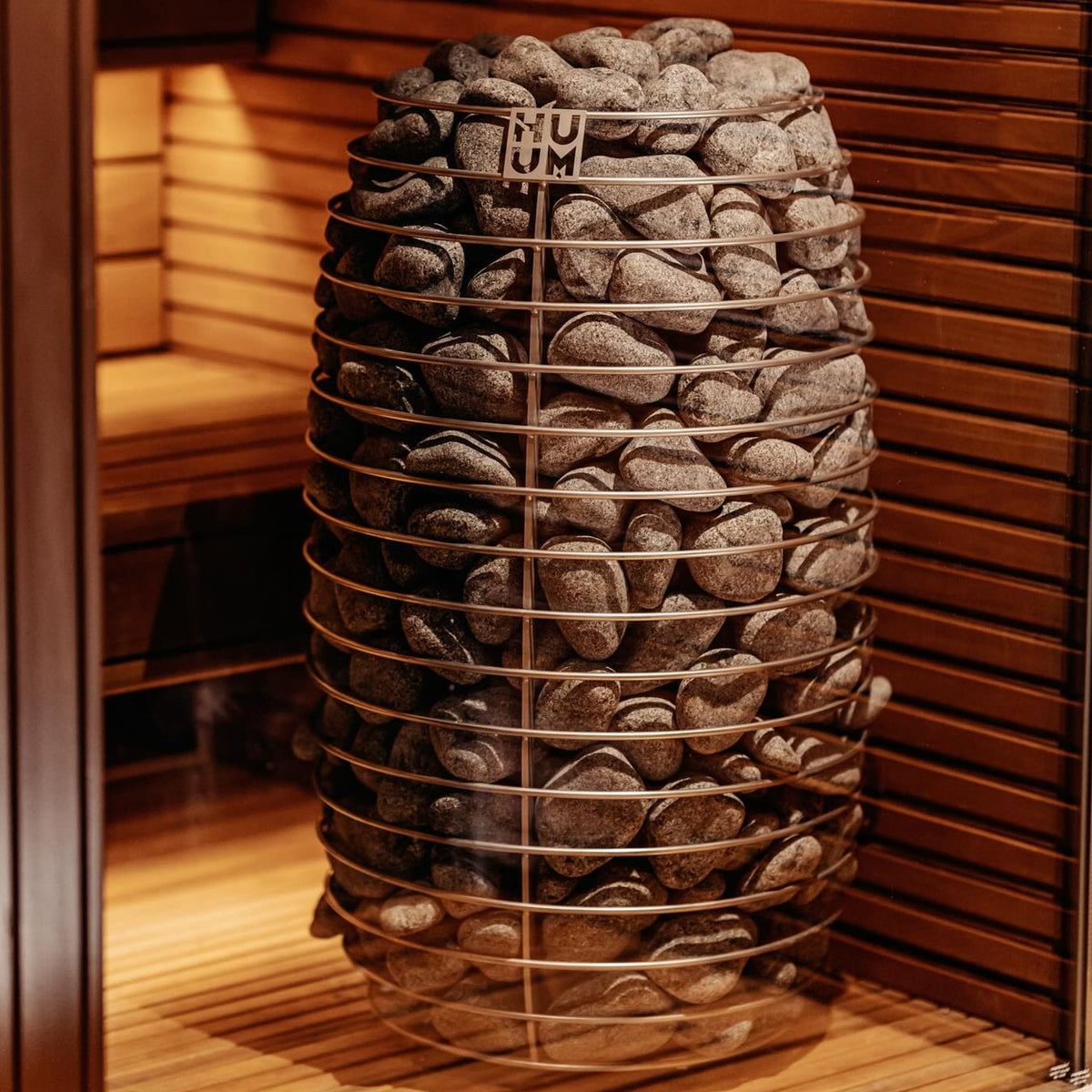 Close-up of electric sauna heater with dark stones and protective wire cage