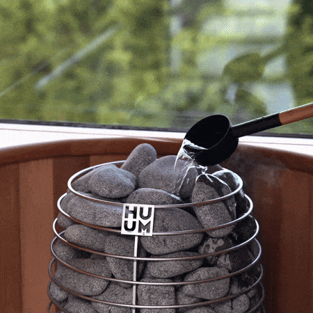 Water pouring onto gray sauna stones in a sauna heater basket